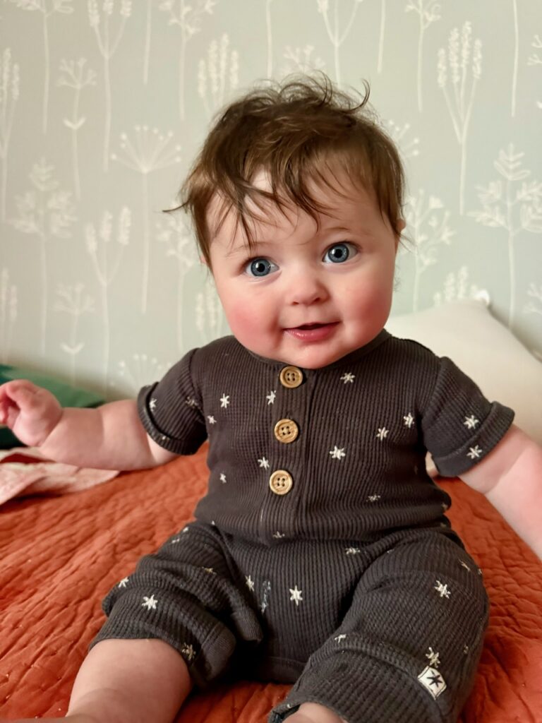 A baby with blue eyes and brown hair sitting up